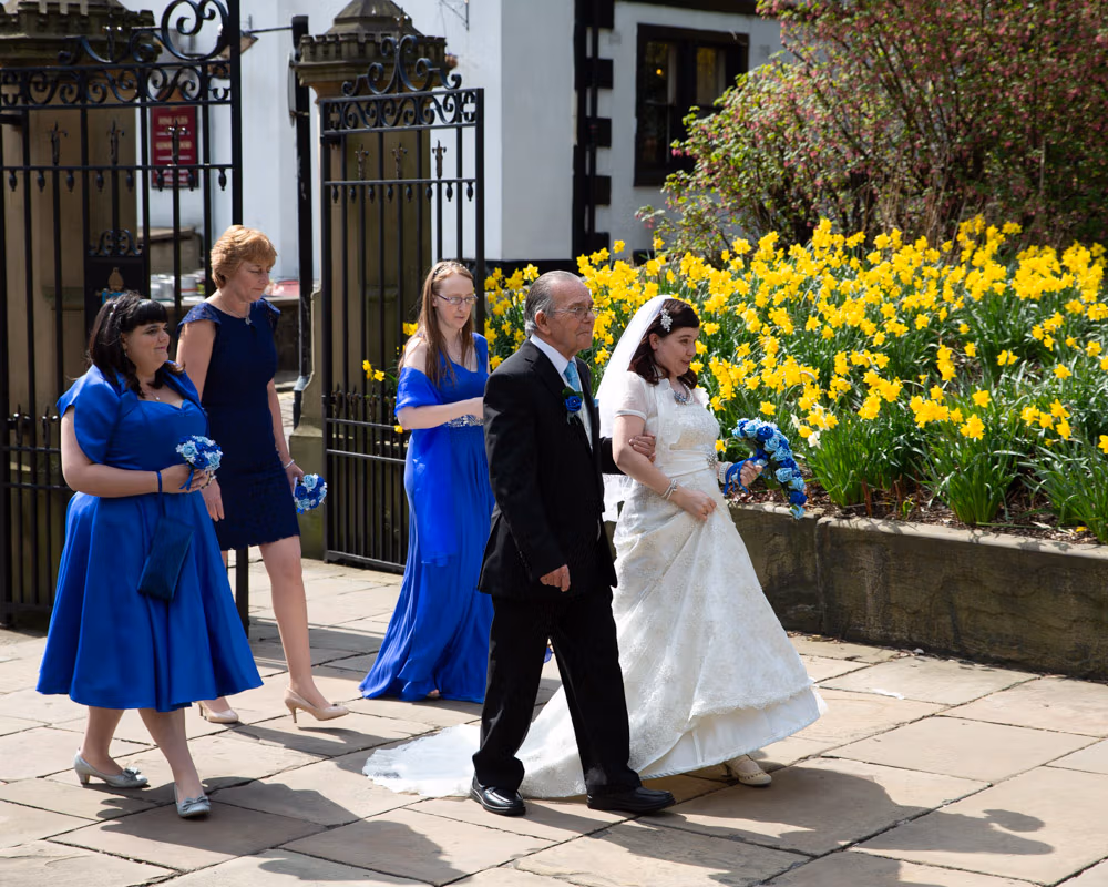 Bride and her father walk along the path, bridesmaids following behind
