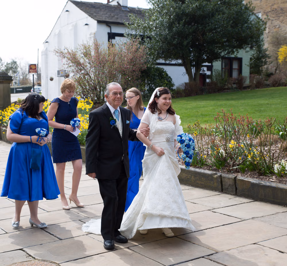 Bride and her father smile as she carefully walks in her dress