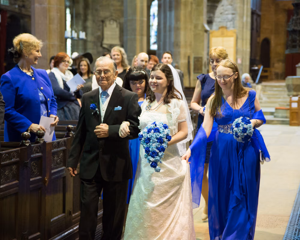 Bride and father followed by bridesmaids, halfway down the aisle, glowing with smiles