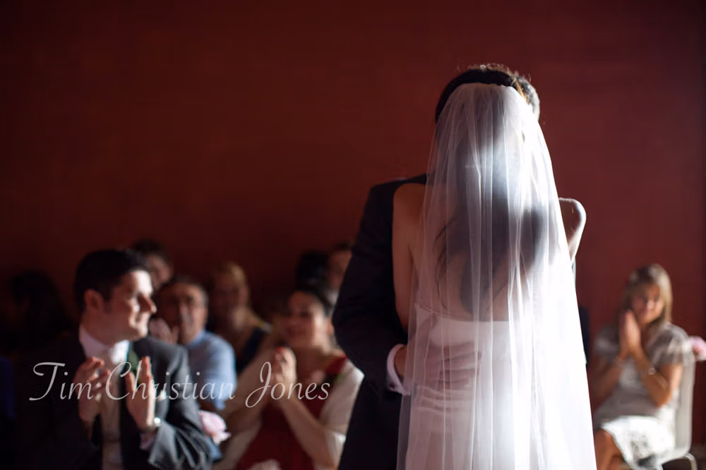 Bride and groom share their first kiss in colour as guests applaud during the ceremony