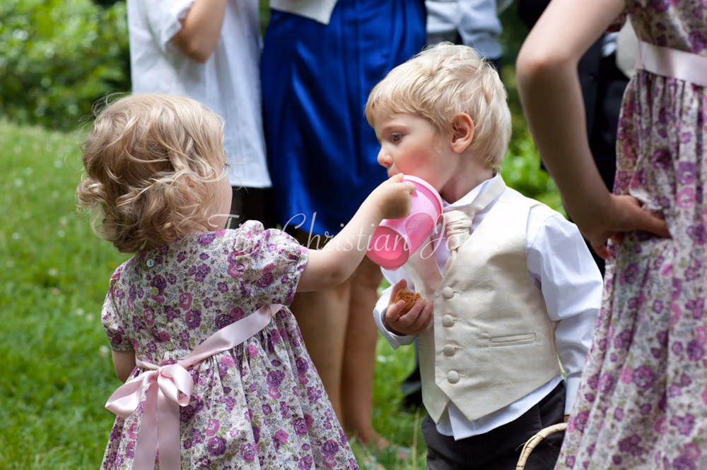 Flower girl offers her sippy cup to the couple’s young son in the garden