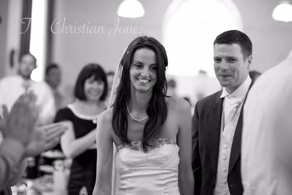 Black and white image of bride and groom walking through the reception tables, smiling