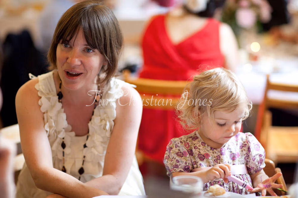 Flower girl colours her fingers with crayons while her mum watches, smiling